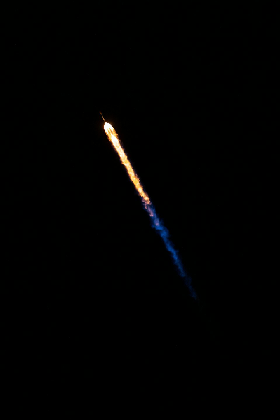 Rocket launching with bright orange flame against dark sky.