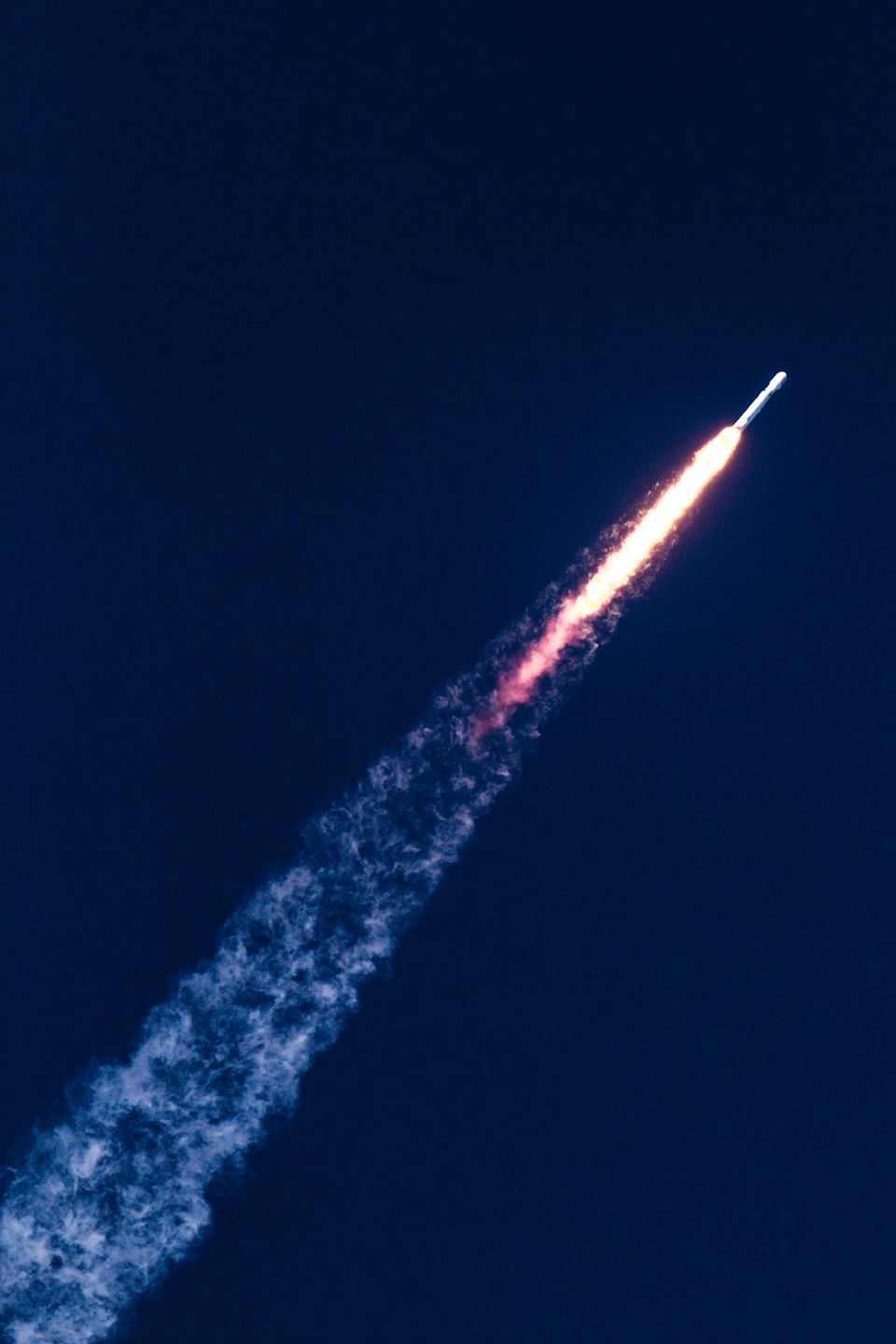 White rocket blasting off into a dark blue night sky.