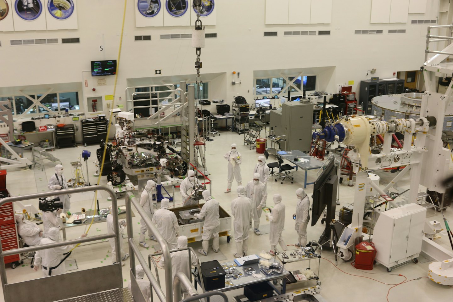 Diverse scientists in cleanroom suits assemble complex machinery.