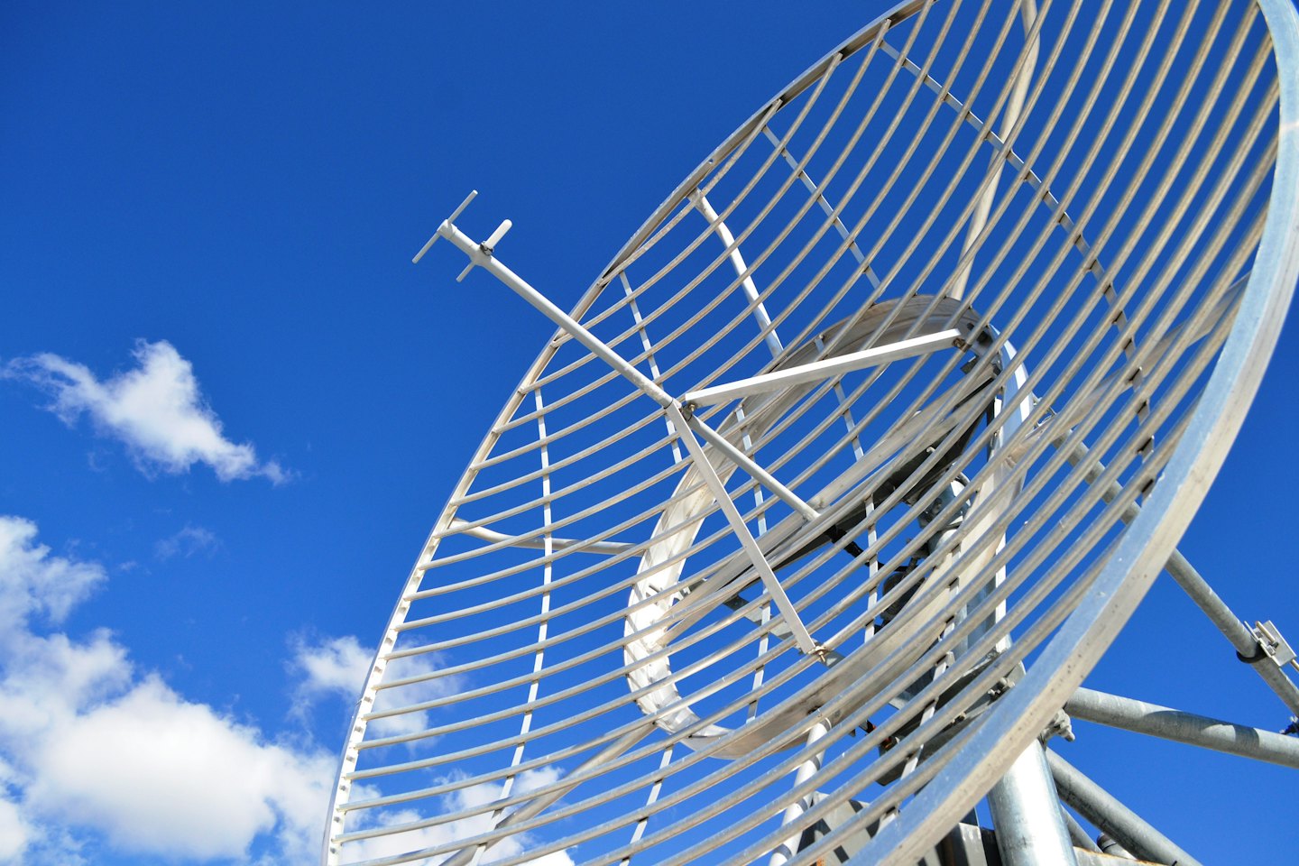 Large metallic satellite dish against a blue sky.